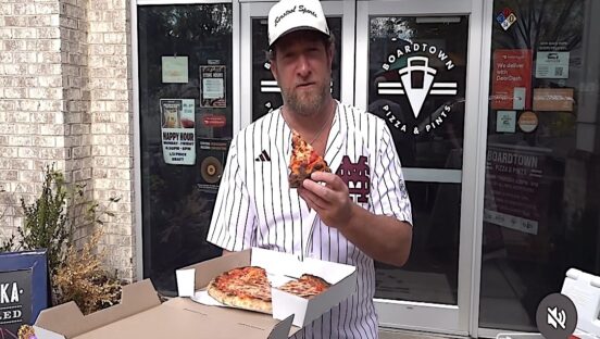 This photo shows Dave Portnoy holding a slice of pizza and standing in front of Boardtown Pizza & Pints in Starkville.