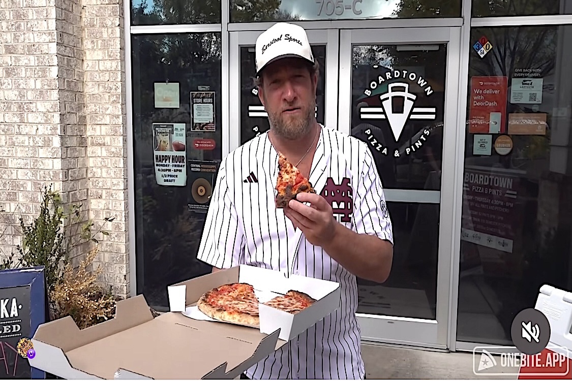 This photo shows Dave Portnoy holding a slice of pizza and standing in front of Boardtown Pizza & Pints in Starkville.