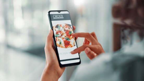 This photo shows a woman's hands tapping on a phone screen that shows the online ordering platform for a pizzeria.