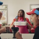This photo shows a smiling Retta holding two Domino's pizza boxes while a pair of employees in the foreground cheer.