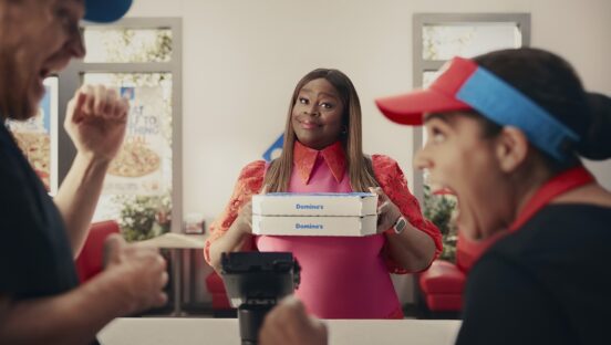 This photo shows a smiling Retta holding two Domino's pizza boxes while a pair of employees in the foreground cheer.