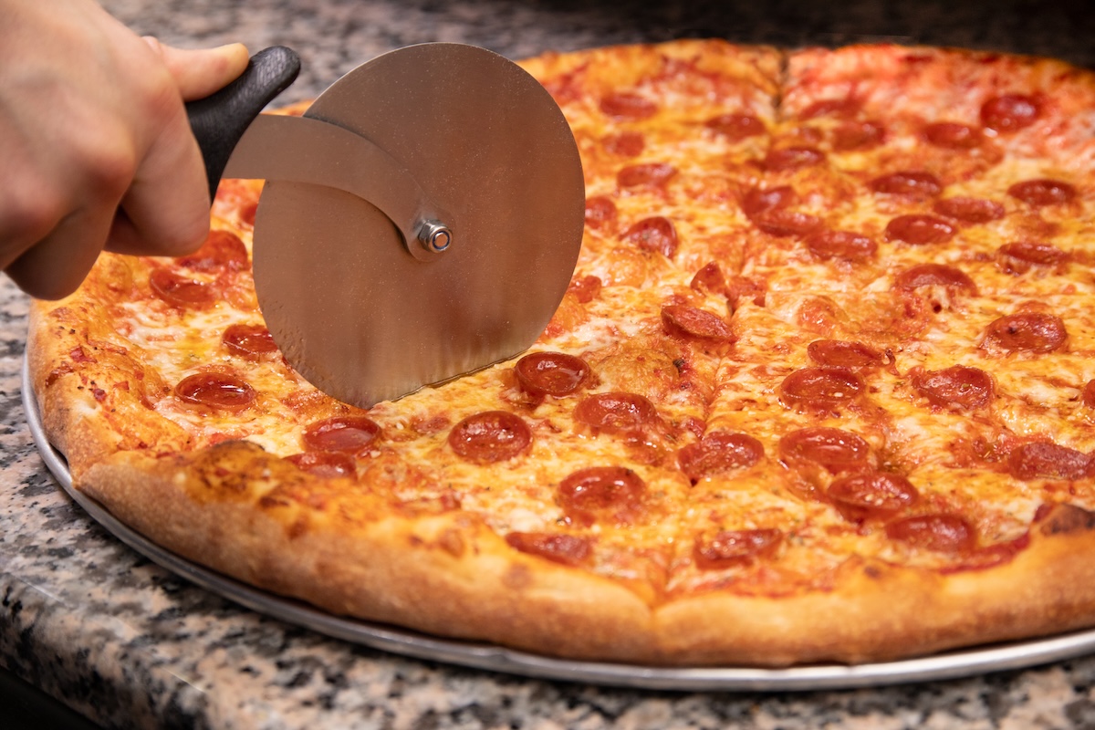 This photo shows a New York-style pepperoni pizza being sliced by a metal slicer.