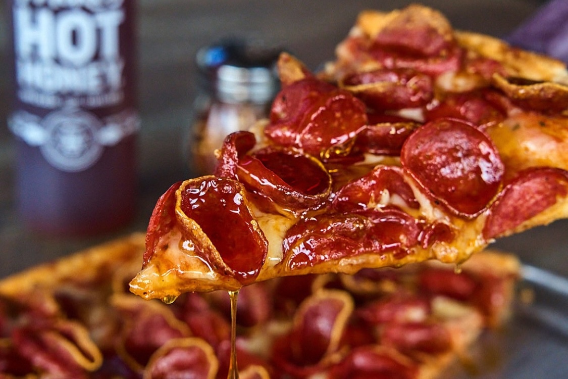 This photo shows a slice of pepperoni pizza with what appears to be a drizzle of hot honey dripping off the edge.