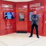 This photo shows Appetronix's Nipun Sharma standing with his arms crossed in front of a dark-red robotic Donatos Pizza location.