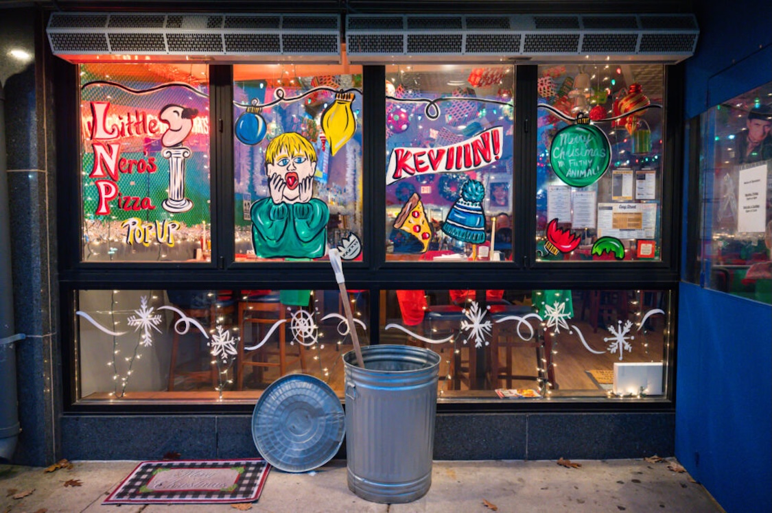 This photo shows some of the Home Alone-themed decor at Easy Street Pizza, including window murals showing little Kevin McAlister, another promoting Little Nero's Pizza, and a green Christmas ornament with the words "Merry Christmas Ya Filthy Animal."