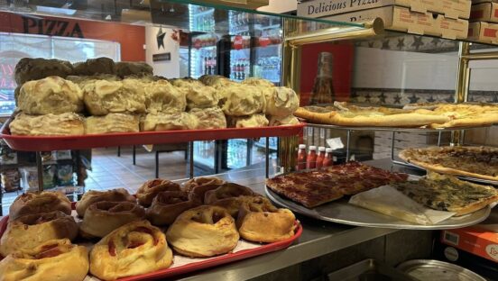 This photo shows several racks of trays loaded with pastries and pizzas in Gara's Pizza.