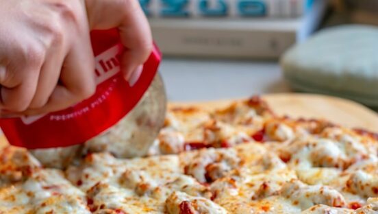 This photo shows a hand slicing a pizza with a red Home Run Inn-branded slicer.