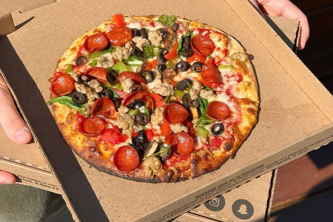 This photo shows a pizza topped with pepperoni, bell peppers, black olives and sausage in a pizza box.