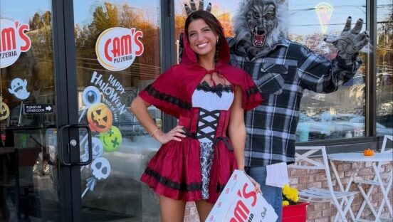 This photo shows Giuliana Calascibetta in a Red Riding Hood costume for Halloween with a man dressed as the Big Bad Wolf behind her. They are standing at the entrance to Cam's Pizzeria.
