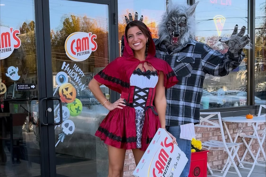This photo shows Giuliana Calascibetta in a Red Riding Hood costume for Halloween with a man dressed as the Big Bad Wolf behind her. They are standing at the entrance to Cam's Pizzeria.