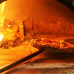 This photo shows a beautiful Neapolitan Pizza being turned around in a blazing wood-fired oven.