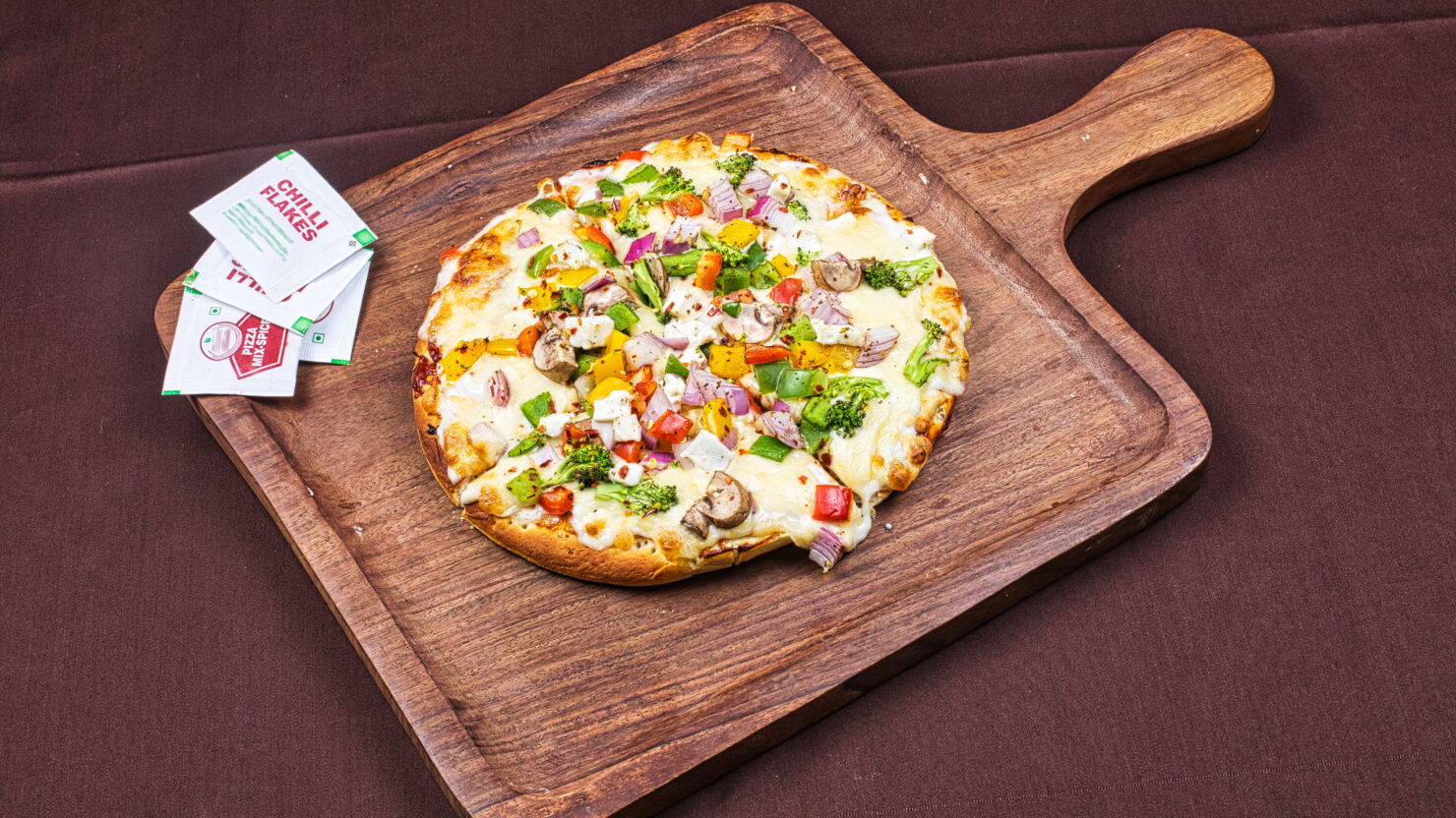 This photo shows a Paneer pizza with vegetables and cheese served on a wooden pizza dish.