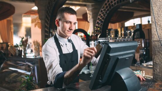 This photo shows a restaurant manager or owner in a white shirt and black apron swiping a credit card through his POS system.