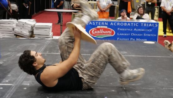 This photo shows a young man on his back, spinning dough between his legs.