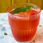 This photo shows the red-colored Pepperoni Pizza Negroni in a glass with a basil leaf.