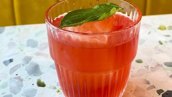 This photo shows the red-colored Pepperoni Pizza Negroni in a glass with a basil leaf.