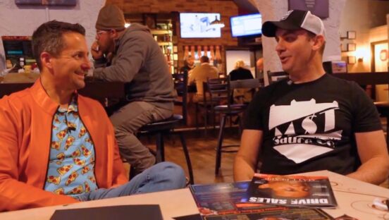 This photo shows Matt Plapp, wearing his trademark orange jacket, sitting at a table with a restaurateur client.