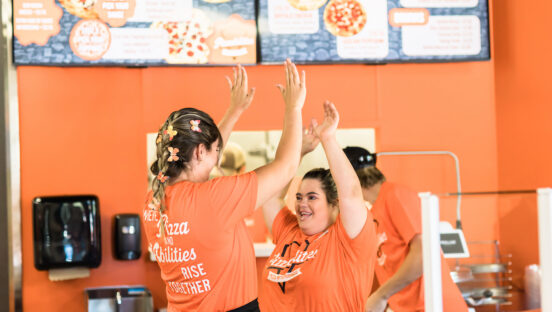 This photo shows Grace Baker high-fiving a fellow team member, both dressed in Pizzabilties' signature orange and black colors.