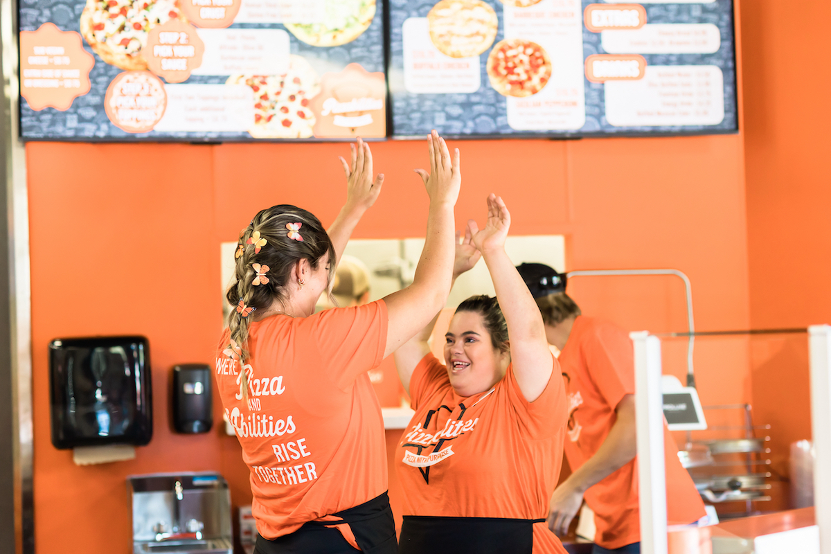 This photo shows Grace Baker high-fiving a fellow team member, both dressed in Pizzabilties' signature orange and black colors.