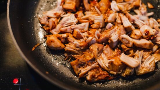 This photo shows shredded jackfruit and shredded chicken sautéing together in a pan.