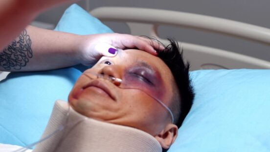 This photo shows an injured man in a hospital bed. The doctor is checking his eyes with a flashlight.