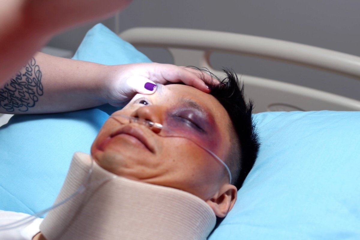 This photo shows an injured man in a hospital bed. The doctor is checking his eyes with a flashlight.