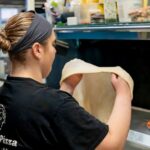 This photo shows co-owner Gena Di Paolo stretching dough in the kitchen at Geno D's.