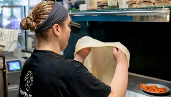 This photo shows co-owner Gena Di Paolo stretching dough in the kitchen at Geno D's.