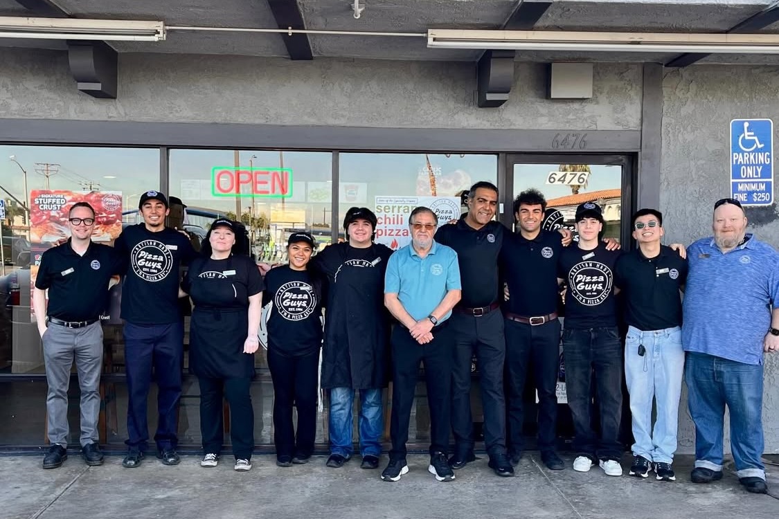 This photo shows a group of employees in front of a newly opened Pizza Guys location.