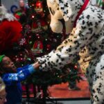 This photo shows a person in a Dalmatian-themed mascot costume holding hands with a happy-looking girl wearing a Santa hat at a holiday party.