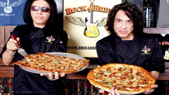 This photo shows Gene Simmons and Paul Stanley, both dressed in black, holding two pizzas.