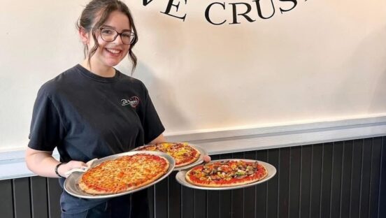 This photo shows Angelina holding two pizzas in the dining room at her pizzeria.