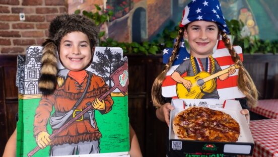 This photo shows two young boys wearing "pizza bibs" - one in a Willie Nelson theme with pigtails and the other wearing a Davy Crockett-style coonskin cap.