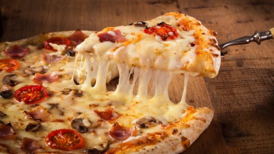 This photo shows a hot pizza slice with melting cheese on a rustic wooden table.