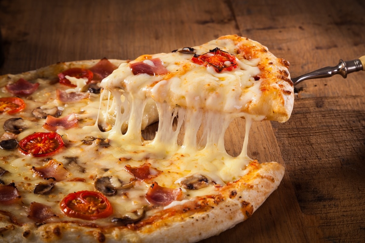 This photo shows a hot pizza slice with melting cheese on a rustic wooden table.