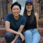 This photo shows Emily Kwak and Christina Cord sitting side by side on the stoop of a house.