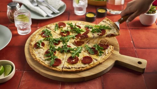 This photo shows a gluten-free pizza topped with dairy-free cheese, pepperoni and arugula.