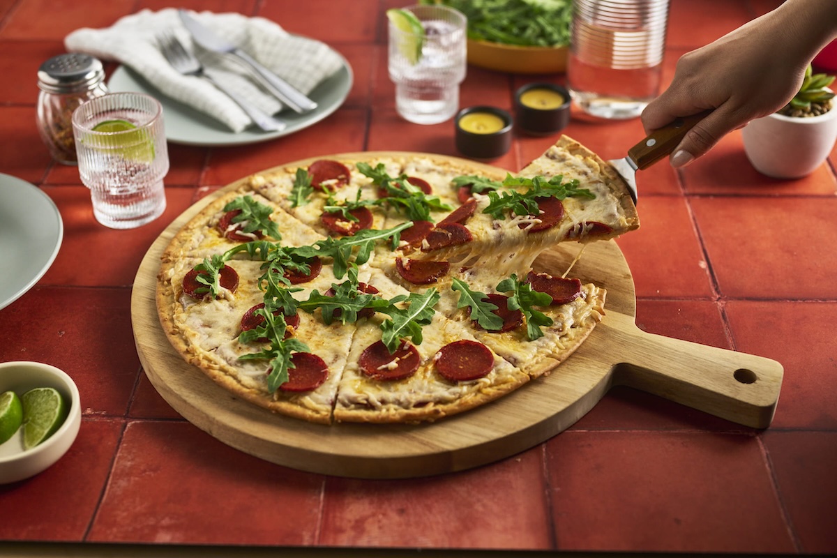 This photo shows a gluten-free pizza topped with dairy-free cheese, pepperoni and arugula.