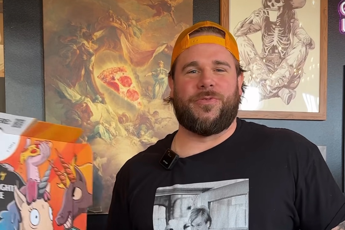 This photo shows Jordan Faeth in a black Chris Farley t-shirt and backwards orange cap standing in a Mikey's location.