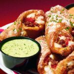 This photo shows a sausage roll from Mellow Mushroom served in a plate with a side of dipping sauce.