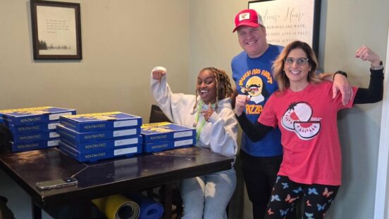 This photo shows the owners of Much Ado About Pizza and another young woman who is sitting at a table piled high with delivered pizza boxes.