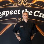 This photo shows Tony Gemignani, hands on hips, standing front of a giant mural with the words "Respect the Craft"