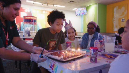 This photo shows a boy blowing out candles on a birthday cake while his friends look on.
