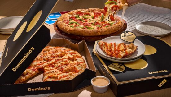 This photo shows a woman's hand removing a slice from a whole Domino's pizza, with other pizzas and slices nearby.