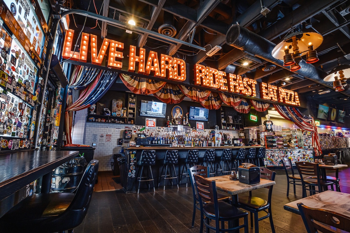 This photo shows the interior of Evel Pie. Above the bar are the words: Live Hard. Ride Fast. Eat Pizza.