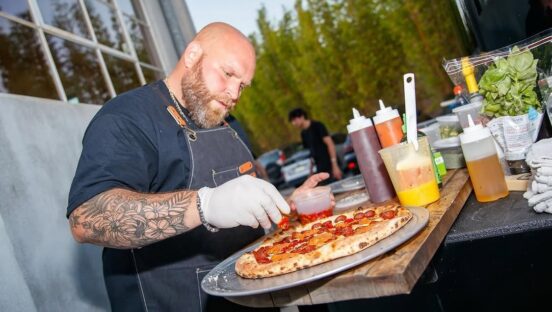 This photo shows Thomas DeSantis adding what appears to be roasted red peppers to a pizza topped with pepperoni.