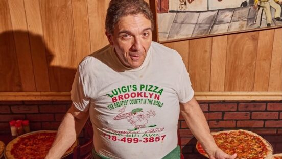 This photo shows Gio Lanzo in his pizzeria with various pizzas on the tables next to him.
