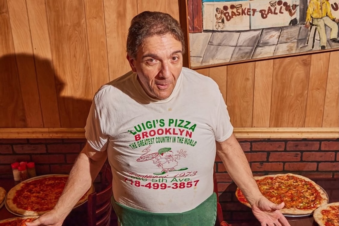 This photo shows Gio Lanzo in his pizzeria with various pizzas on the tables next to him.