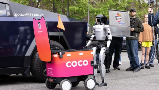 This photo shows a humanoid robot standing next to a Coco-branded pizza delivery bot in front of the Cyber Pizza Truck.