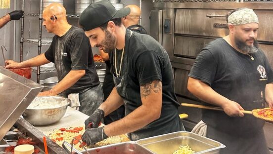This photo shows several men making pizzas in the kitchen at Uncle Rico's.